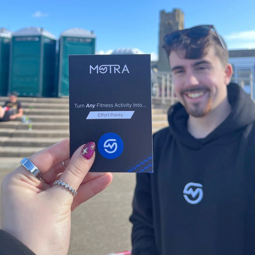 A black MOTRA Effort Points card held in front of a smiling team member wearing a MOTRA hoodie.