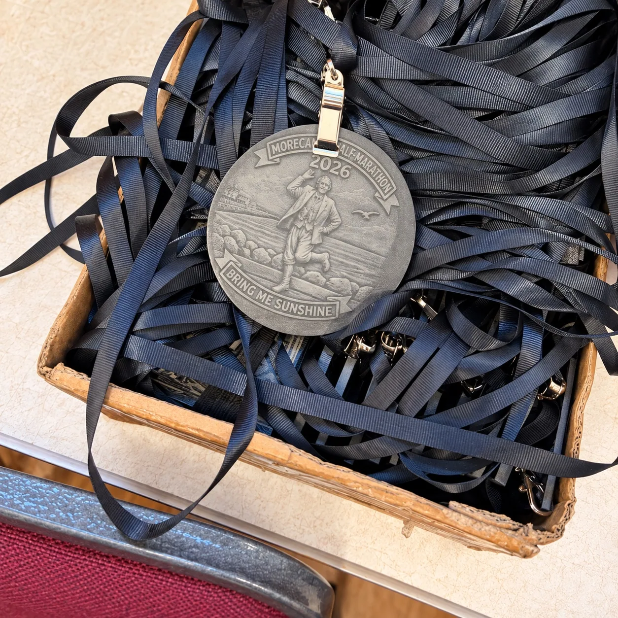 A tray of navy medal ribbons with a 2026 Morecambe Half-Marathon medal on top.