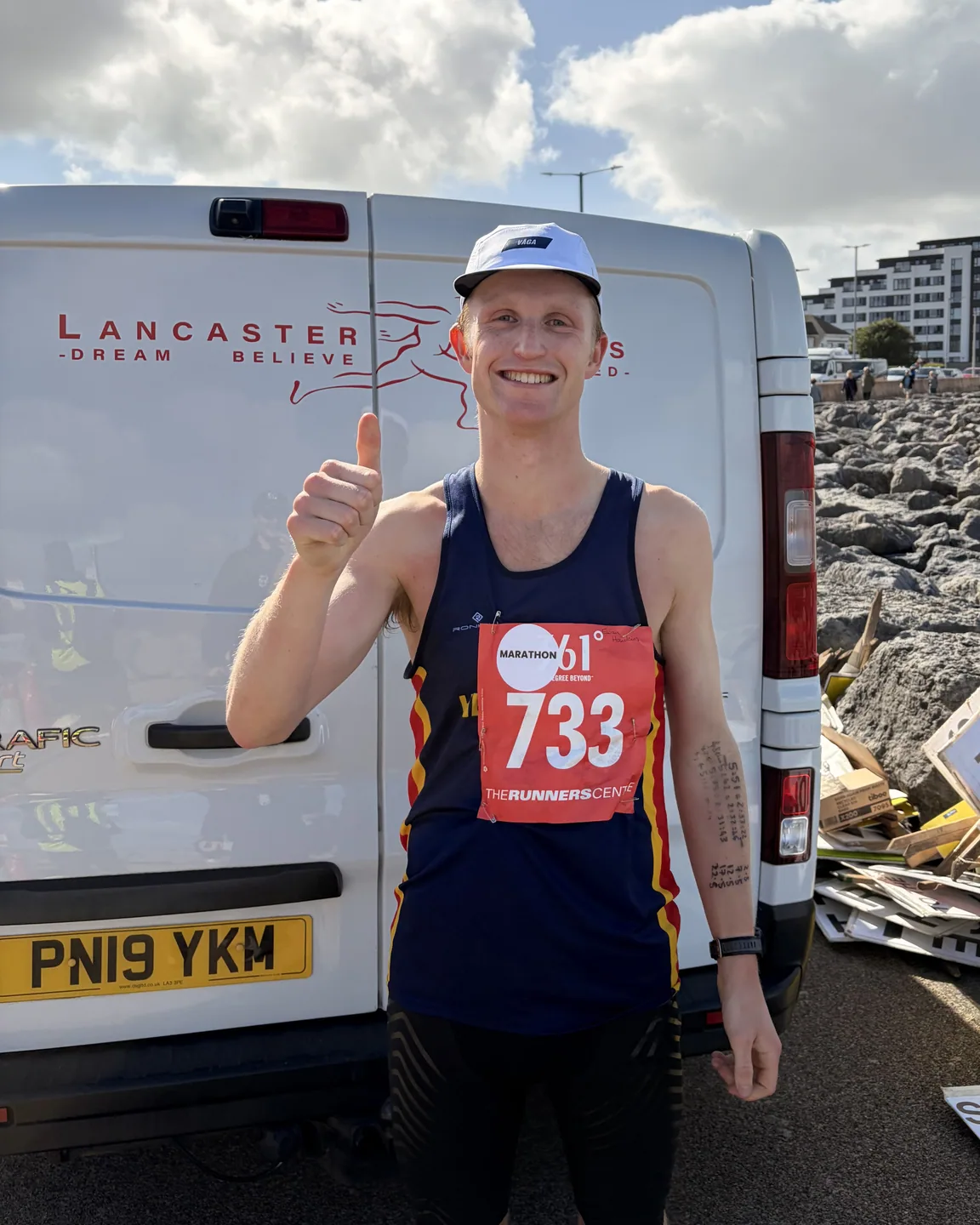 A smiling runner giving a thumbs-up in a white VÅGA cap and race bib at the Morecambe event.