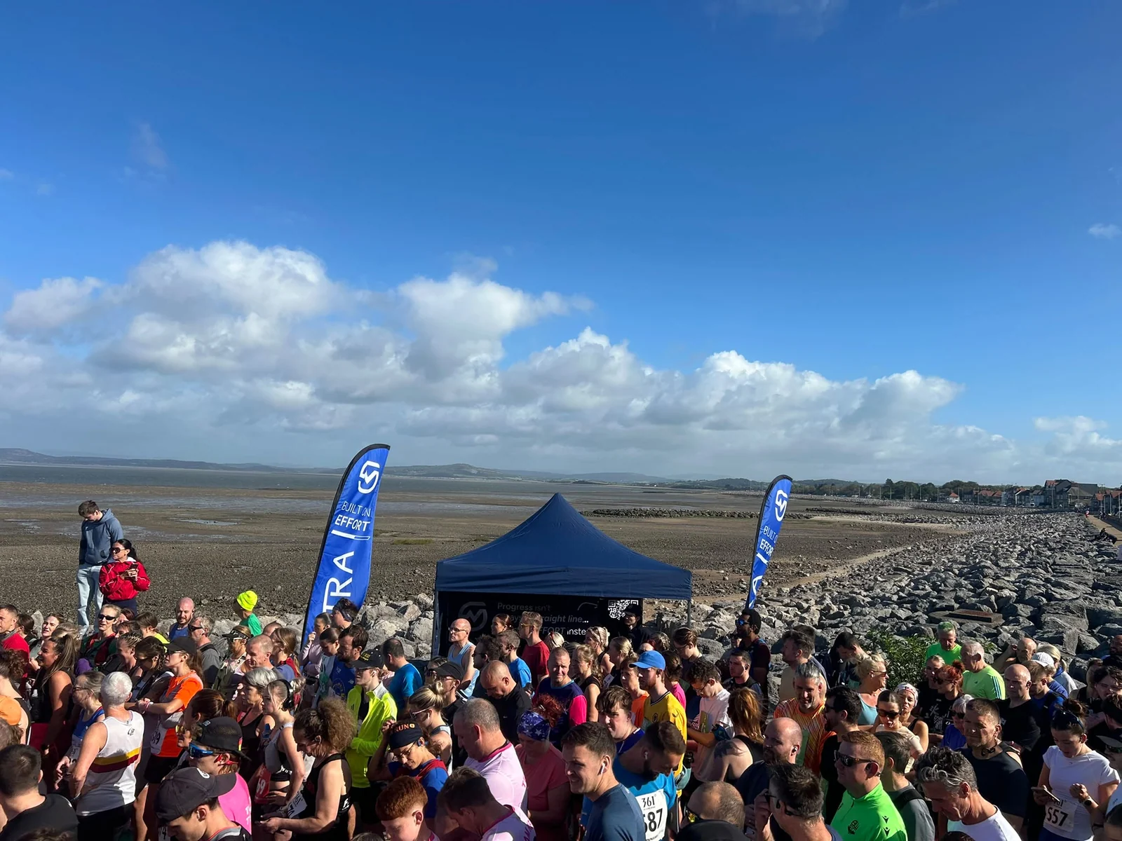 Runners gathered beside the MOTRA stand and blue flags on the Morecambe Bay promenade.