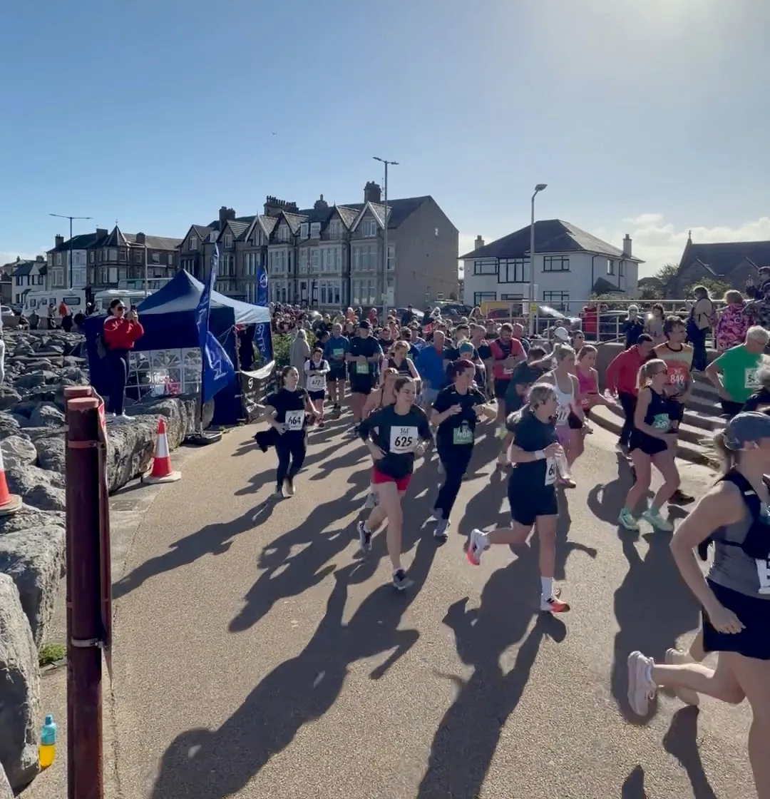 Runners passing the blue MOTRA stand along the Morecambe promenade.