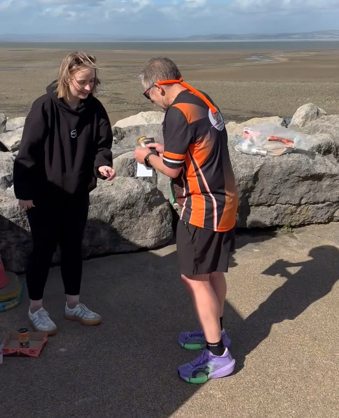 A MOTRA team member speaking with a runner holding a TENZING can and card beside Morecambe Bay.