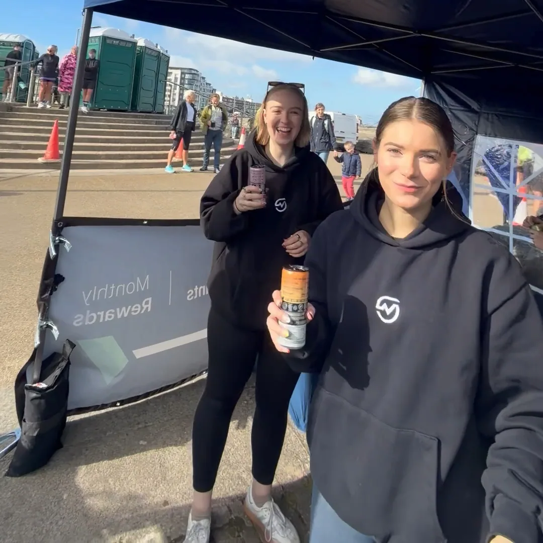 Two MOTRA team members in black hoodies holding TENZING cans beneath the event canopy.