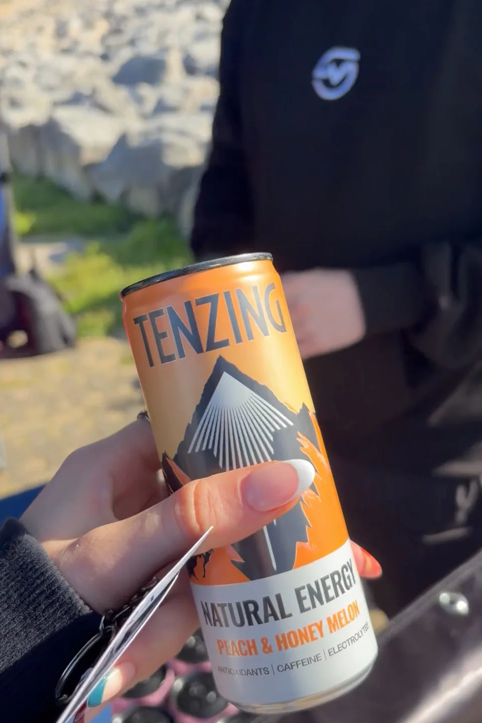 A TENZING Peach & Honey Melon can held in front of a volunteer wearing a MOTRA hoodie.
