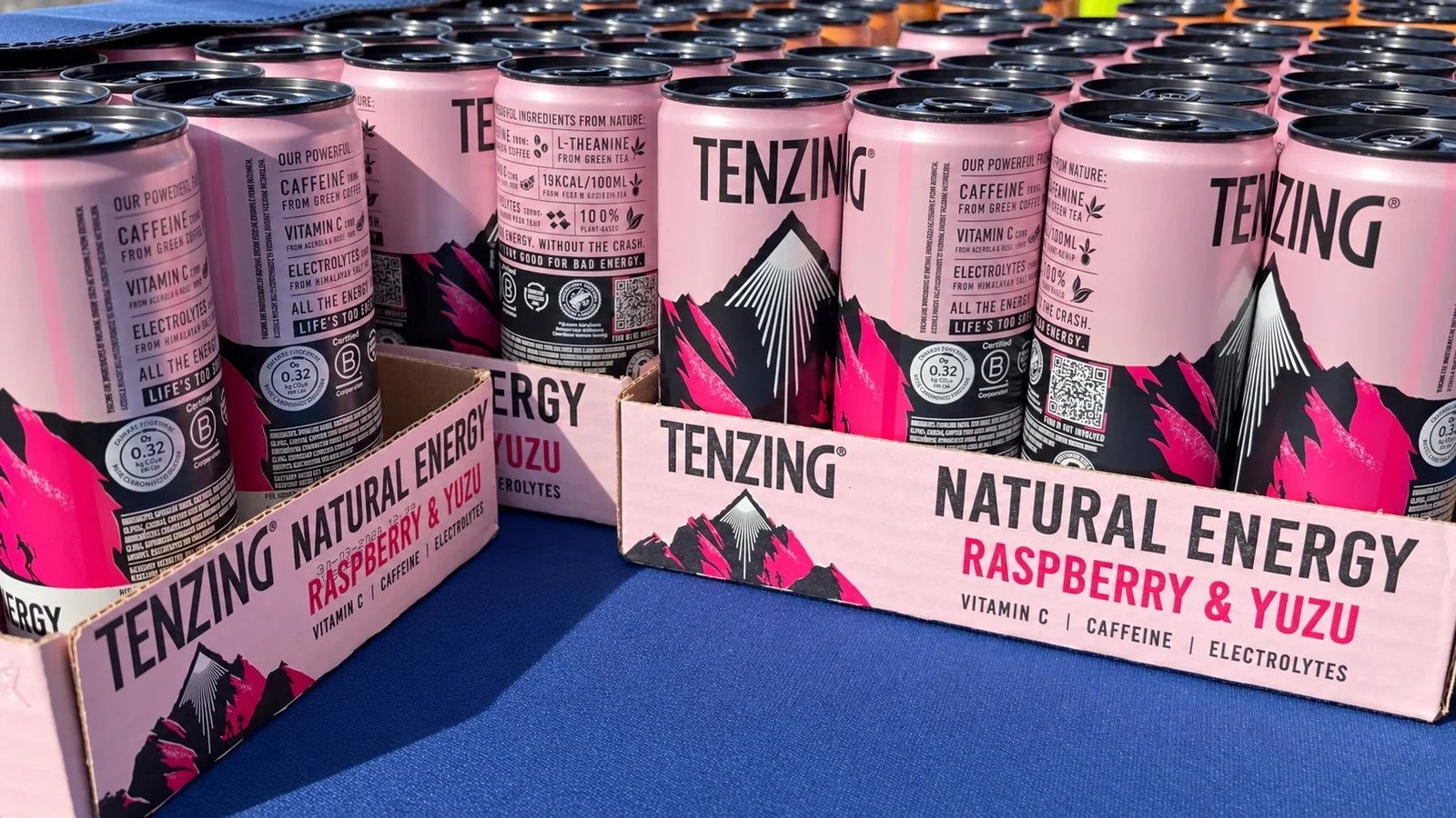 Rows of TENZING Raspberry & Yuzu cans arranged on the blue MOTRA drinks table.